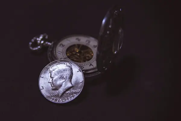 Moeda de prata de dólar americano ao lado de um relógio de bolso
