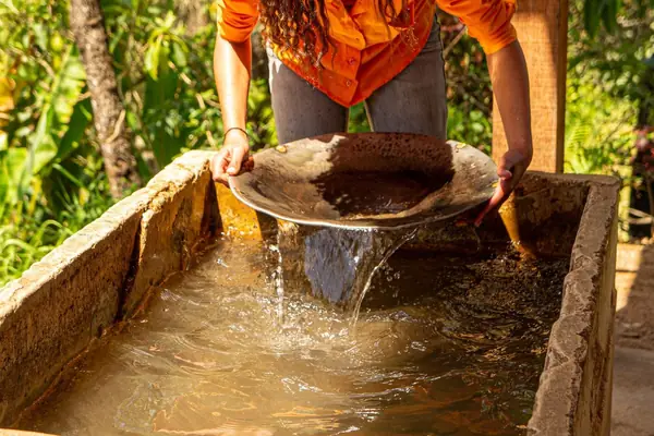 Pessoa peneirando cascalho em uma calha com água