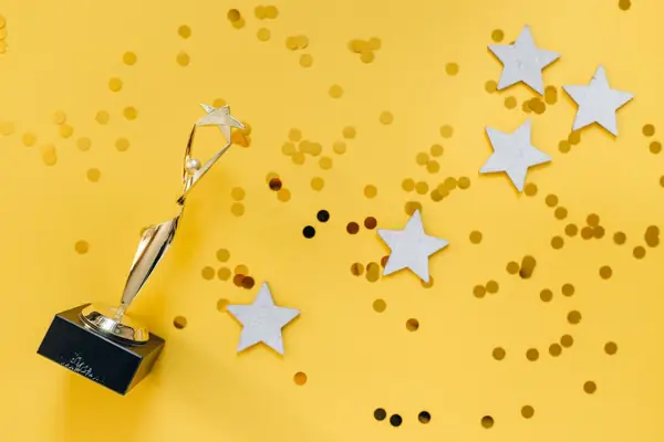 Estatueta dourada e estrelas sobre fundo amarelo