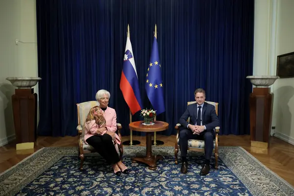 Christine Lagarde sentada ao lado do primeiro-ministro da Eslovênia, diante das bandeiras da Eslovênia e da União Europeia